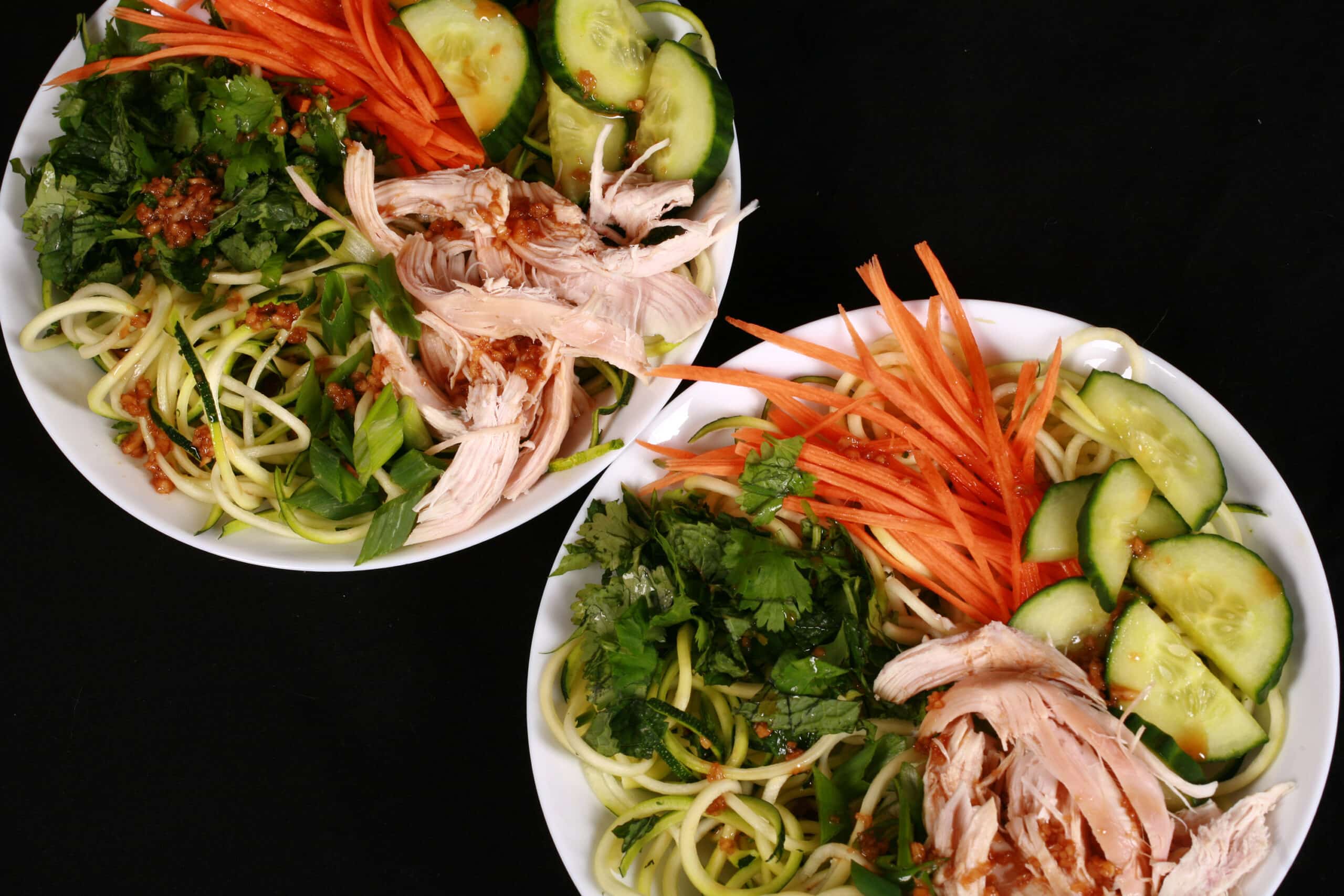 Two bowls of Vietnamese zucchini noodle salads, with zoodles, cucumber, carrot, mint, cilantro, chicken, and dressing.