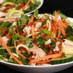 Two bowls of Vietnamese zoodle salads, with zucchini noodles, cucumber, carrot, mint, cilantro, chicken, and dressing.
